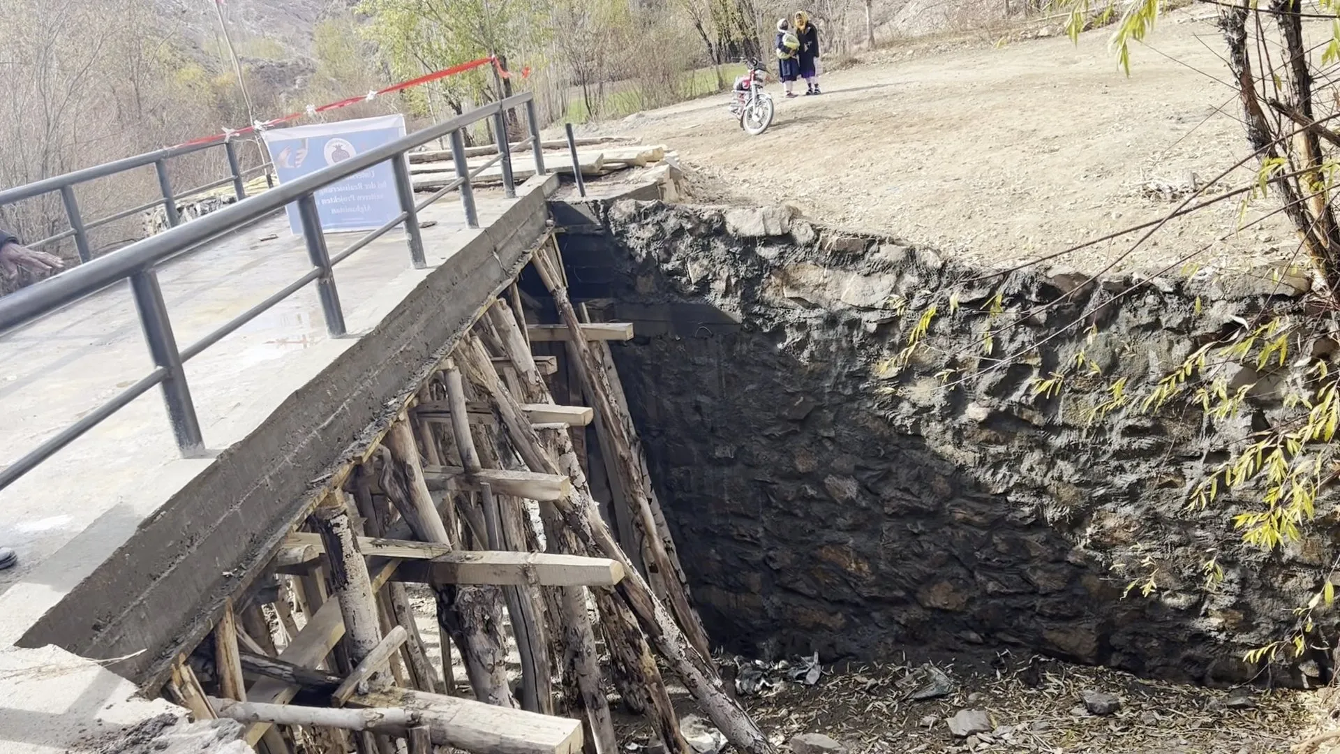Die neue Brücke mit Metallgeländer; darunter steht noch das Holzgerüst der Schalung vor einer Steinmauer.