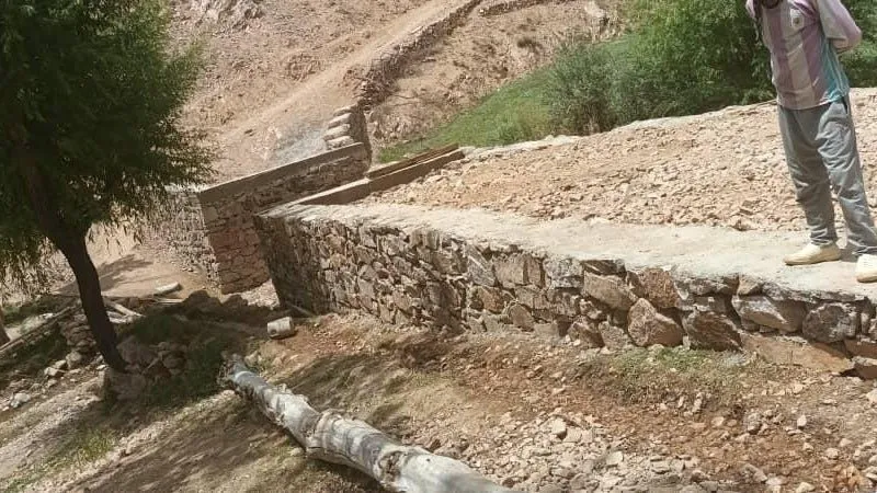 Frisch gemauerte Steinwände und ein aufgeschütteter Zugang zur Brücke; daneben liegt ein Baumstamm, oben steht ein Mann.