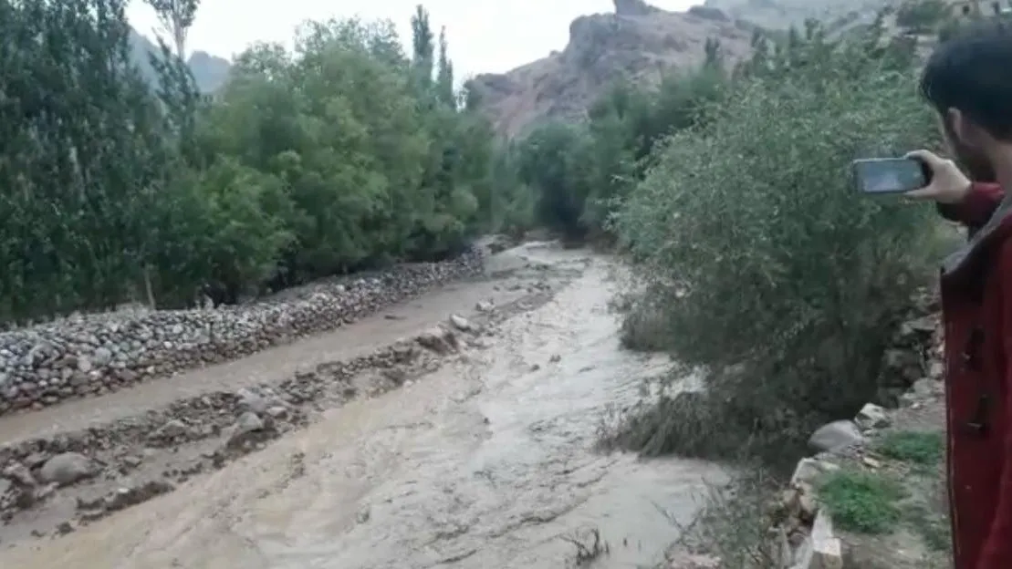 Braunes Hochwasser fliesst zwischen Bäumen und Steinmauern durch das Tal; rechts filmt ein Mann mit dem Handy.