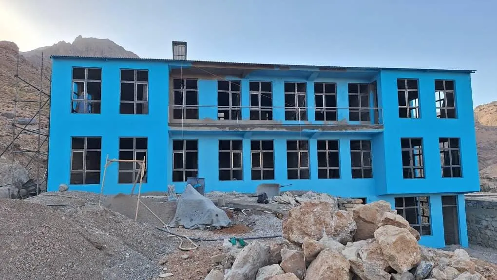 Das neue Schulgebäude in Siaqol mit leuchtend blauer Fassade, davor Baumaterial und Felsbrocken, im Hintergrund karge Berge.